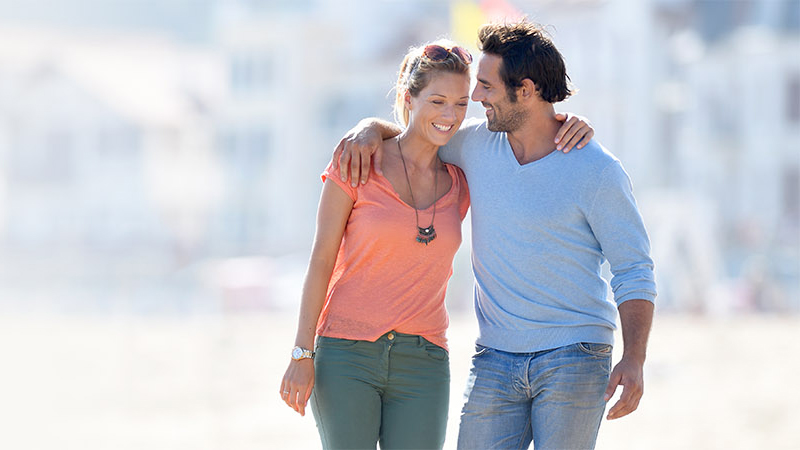 a young couple walking together with their arms over each others shoulders, smiling, after getting HRT in Fort Myers