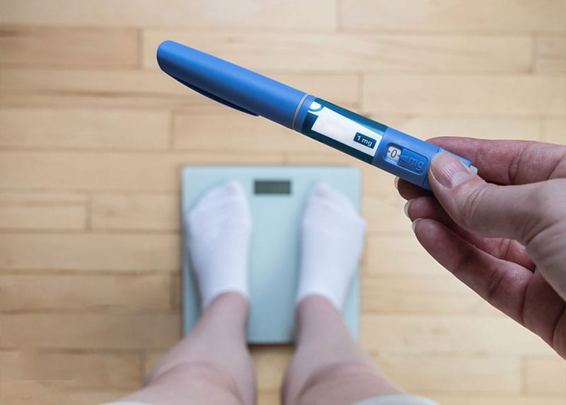 a person standing on a scale and staring at an injectable pen with Semaglutide weight loss in Fort Myers